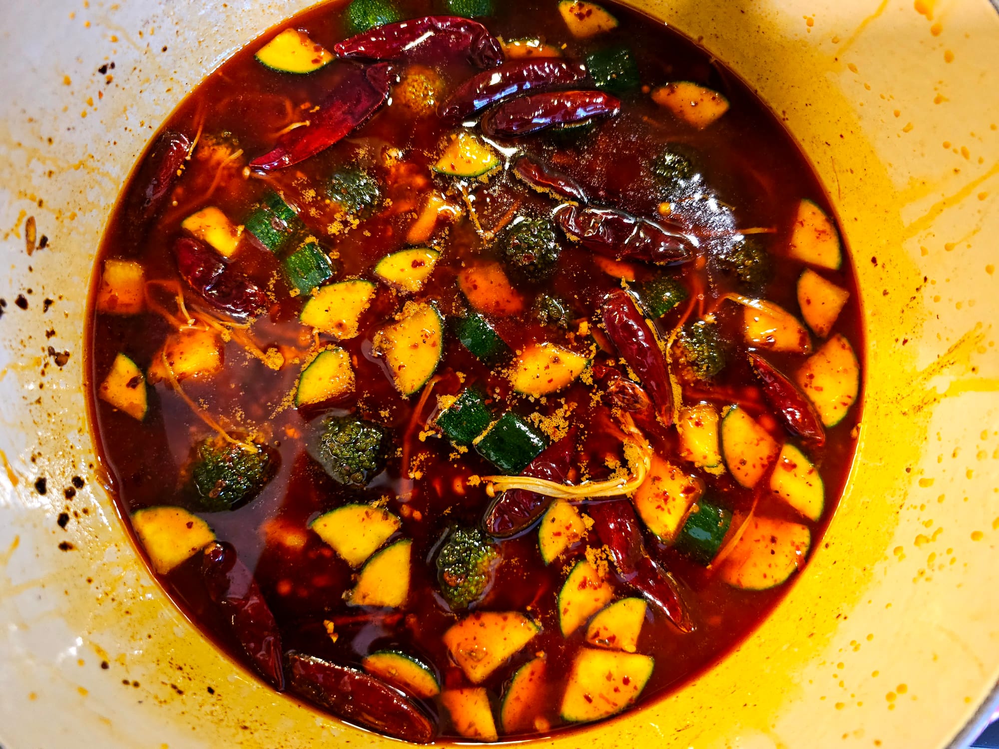Aerial view of a hot-pot, with dark red liquid, all sorts of vegetables and chilis