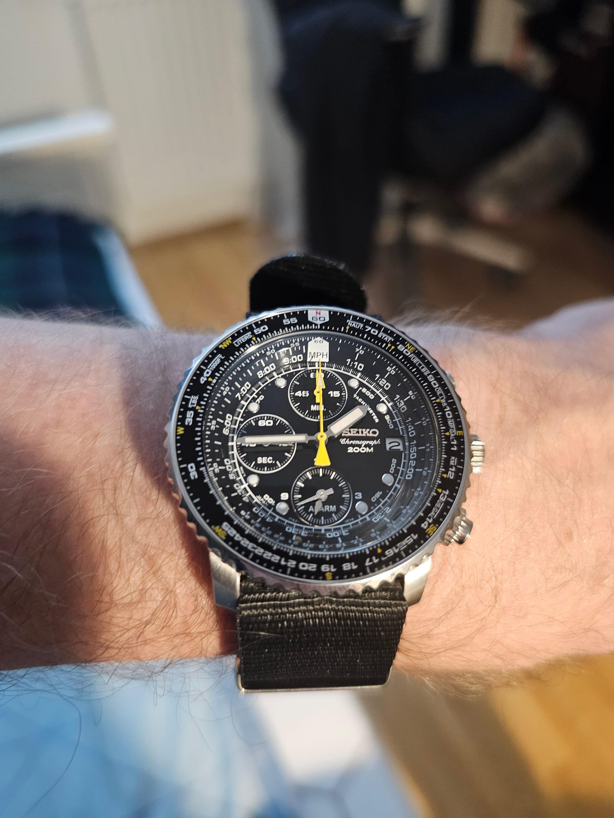 Image of a wrist with the busy dial of a Seiko flightmaster, on a black nato strap. 