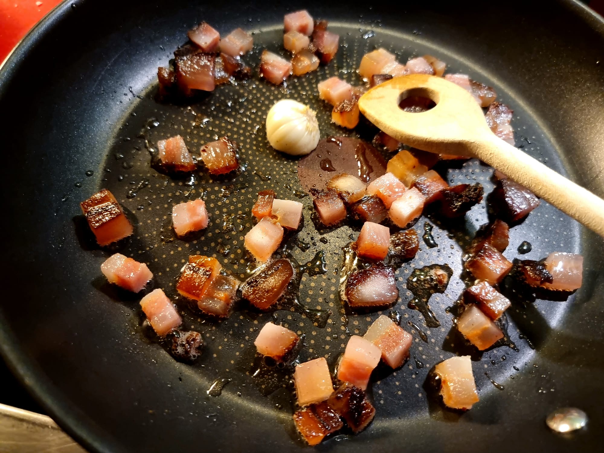 A pan filled with diced bacon and a clove of garlic