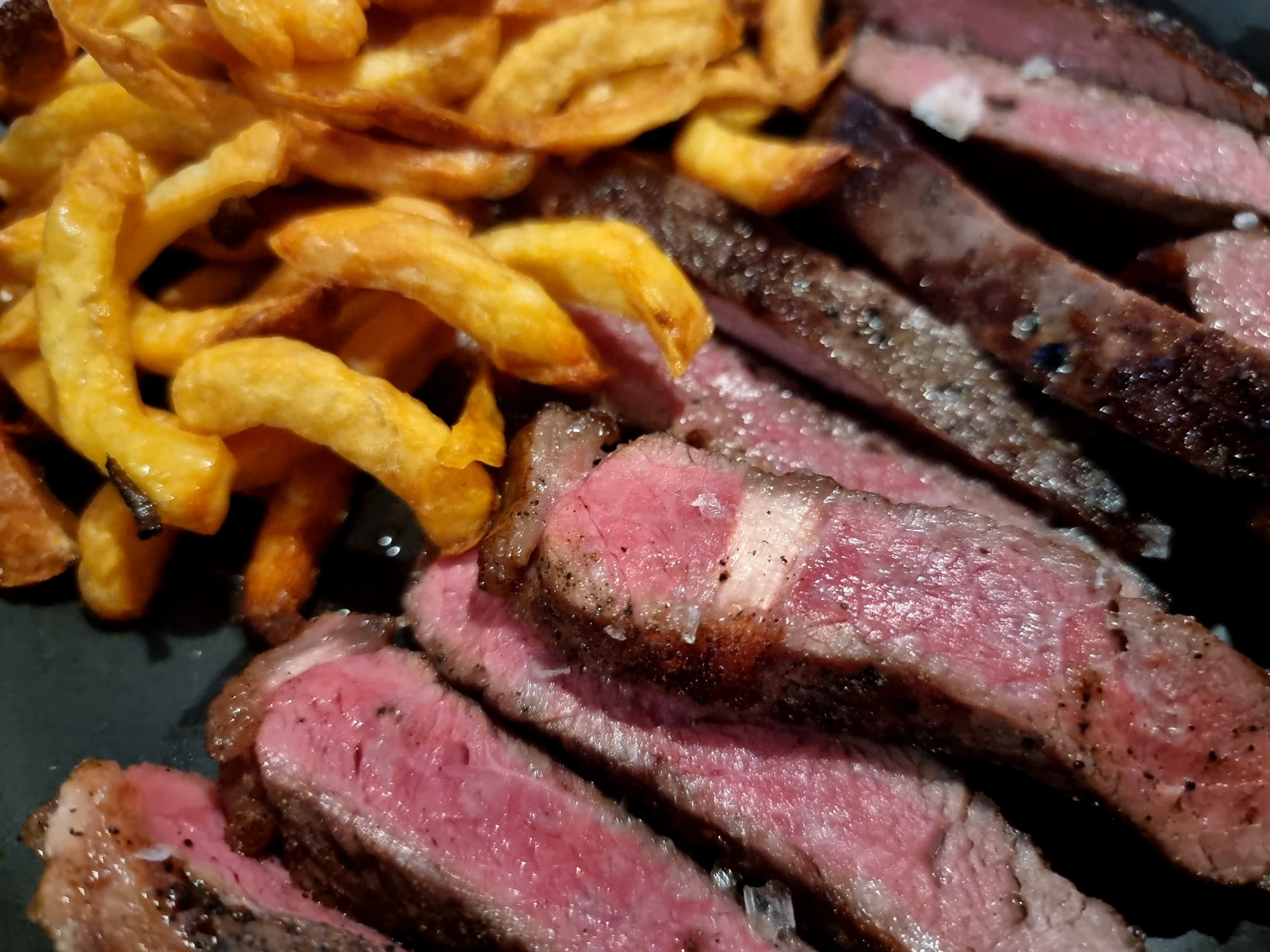 Medium rare steak cut into strips, with a whole bunch of crispy fries