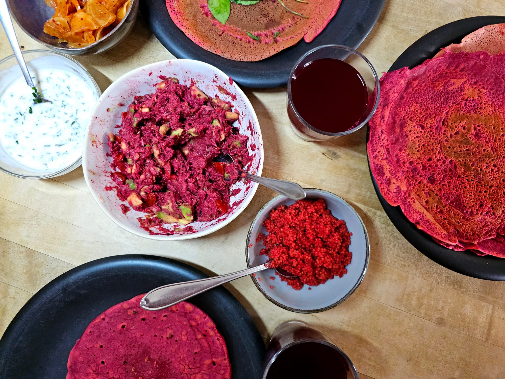 A table with an assortment of dishes coloured red. Beets juice, chickpea pancakes with beets, tuna and avocado mix with beets and sorghum with beets 