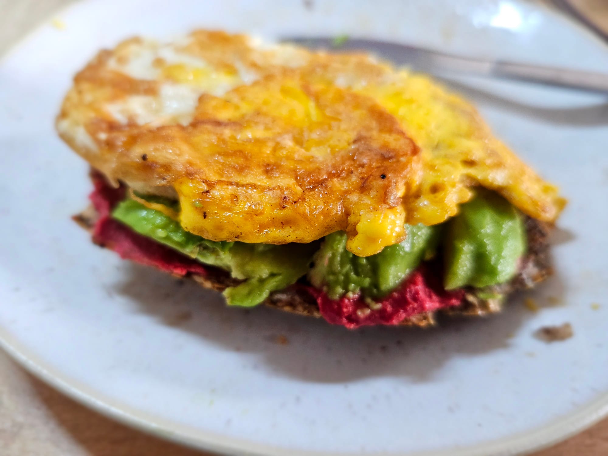 An avocado sandwich with red beets hummus and a fried egg 