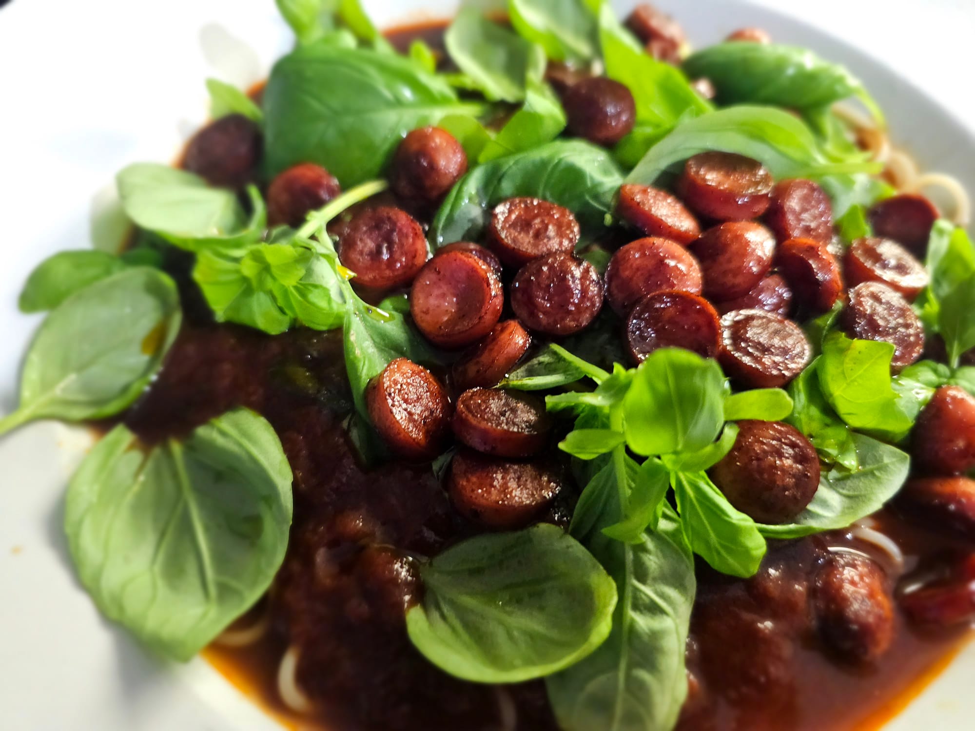 Pasta in a red sauce, garnished with basil and grilled sausage 