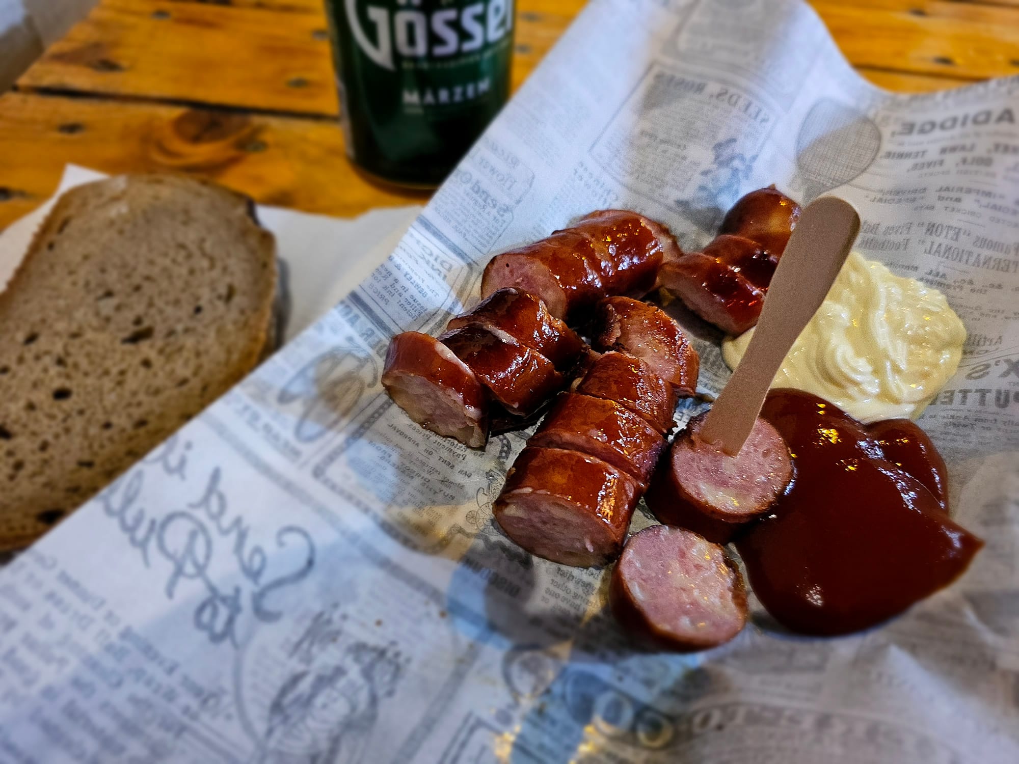 A Käsekrainer, cut into uneven pieces, a slice of bread, ketchup and mayo and a small can of beer 