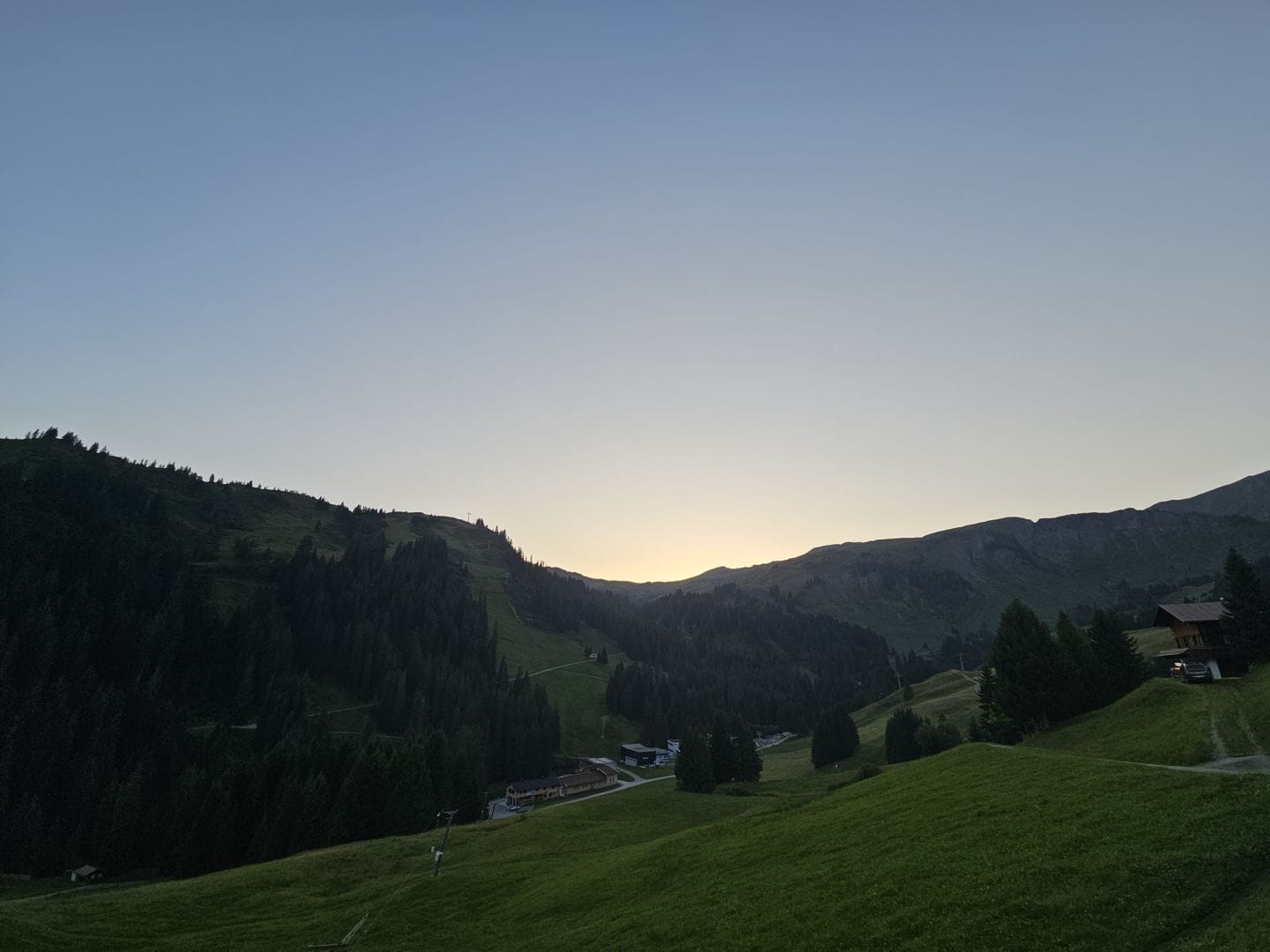 An alpine ridge in the dusk, blue sky with a silver glow. Lots of lush greenery.