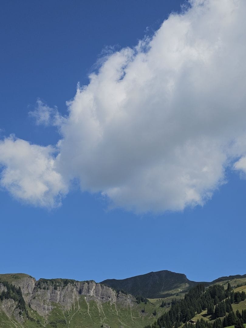A huge chunk of blue skies, with a bulbous white cloud coming in from the right. Below a mountain ridge, partly covered in the cloud's shade
