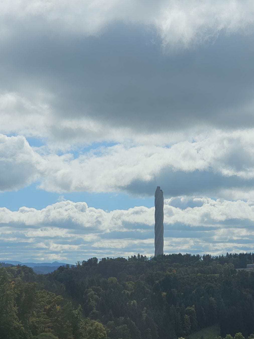 View of a whole lot of trees, with a large monument in the background, against a cloudy sky