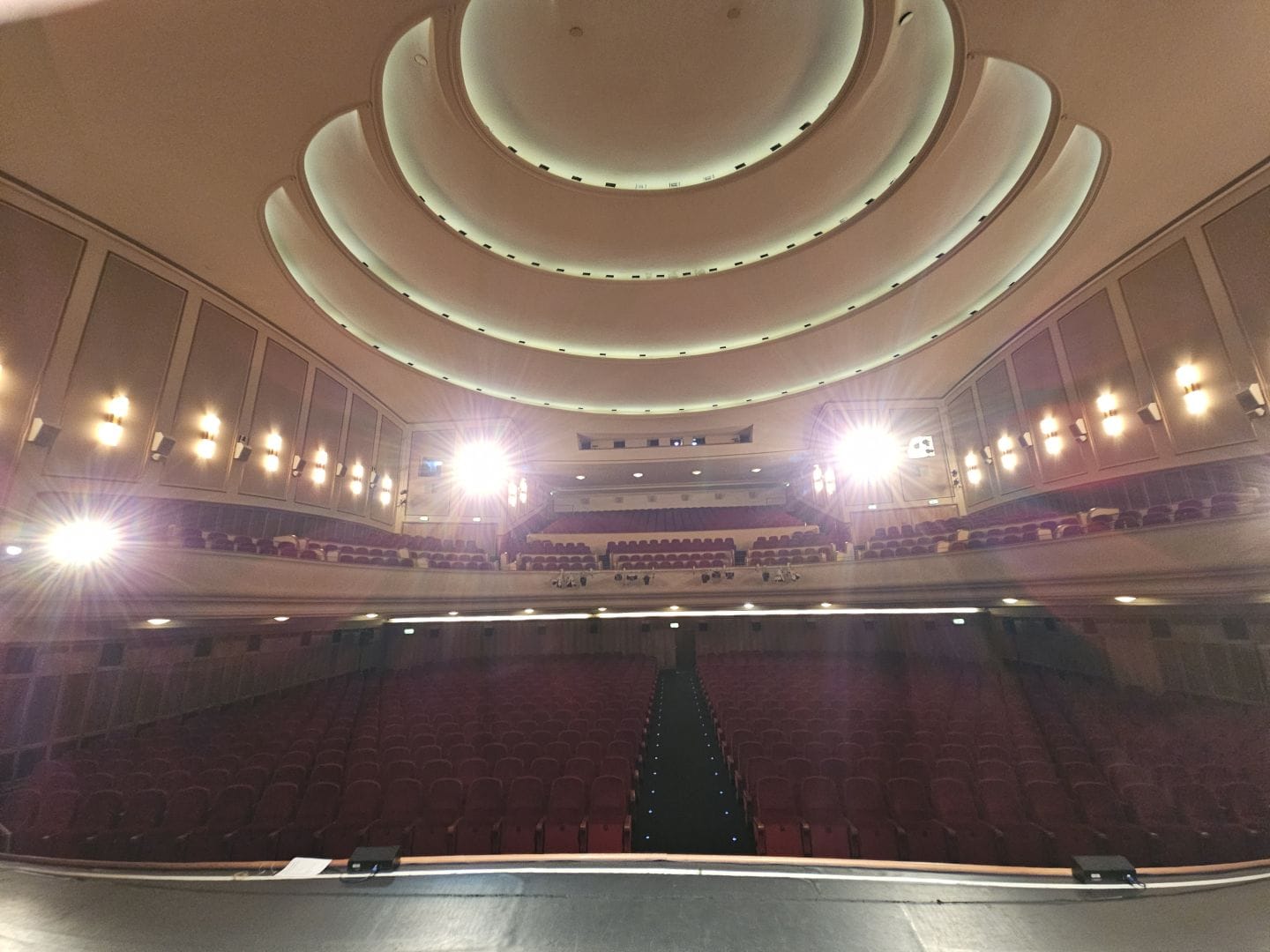 View of an empty Lichtburg in Essen, from the stage. It looks very grand, with deep red, plush seating and impressive lighting.