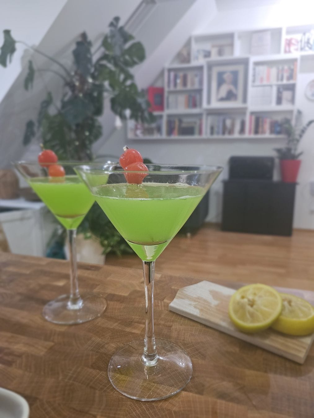 Two cocktail glasses filled with a neon green liquid, two maraschino cherries as garnish.