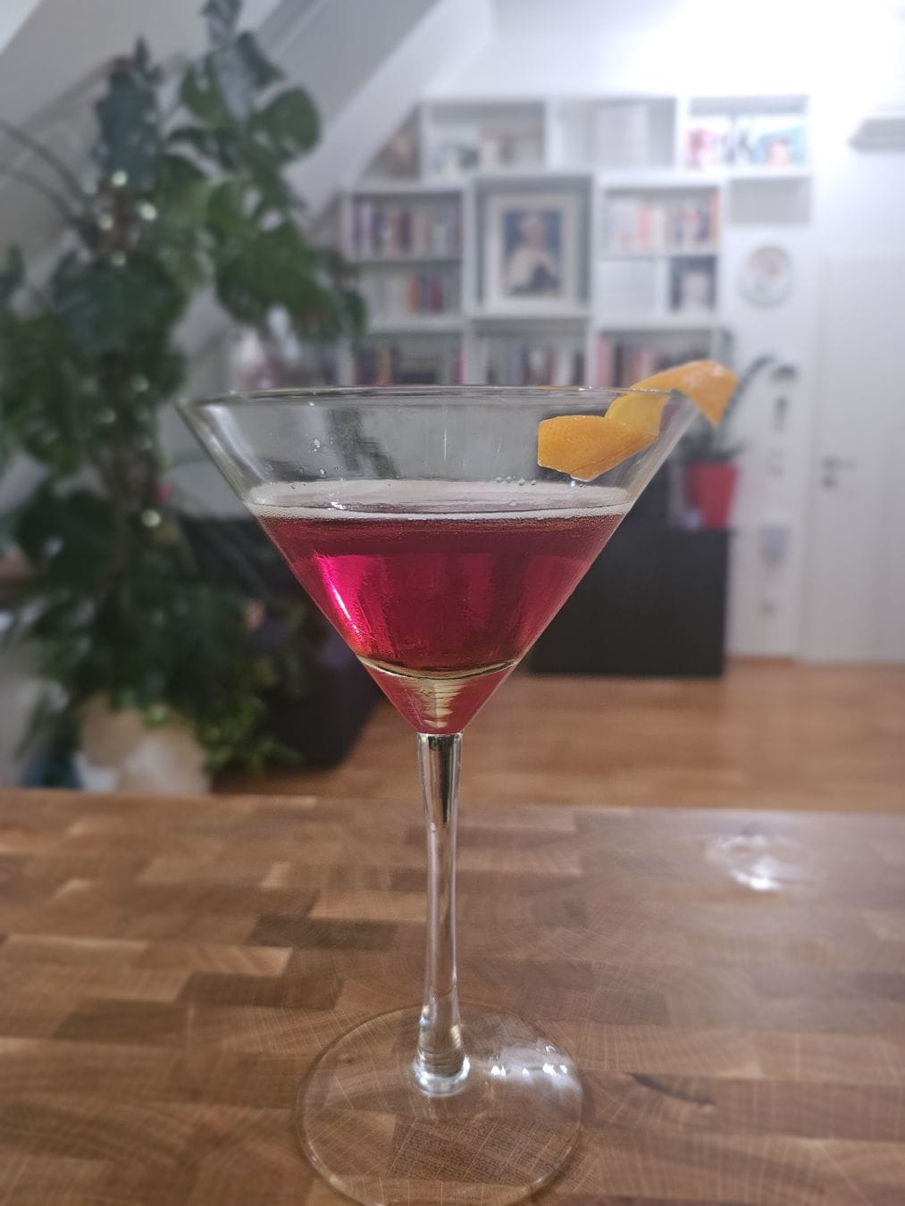 Cocktail glass filled with a reddish liquid, garnished with an orange peel.