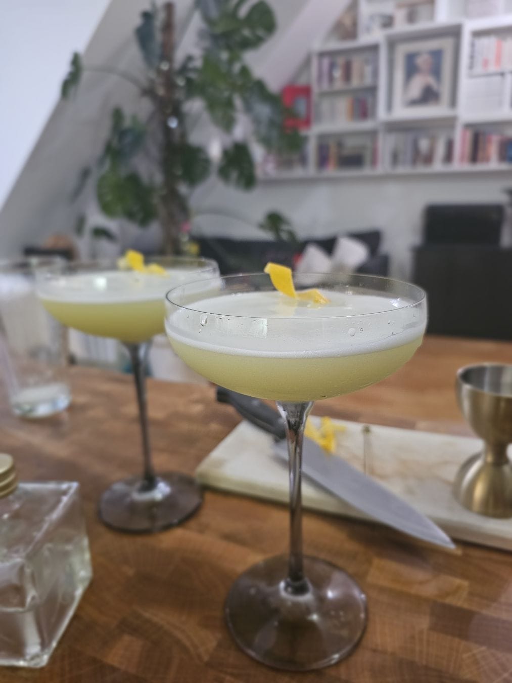 Two cocktail glasses filled with a yellowish liquid, a thin layer of foam on top. Lemon twist in each glass as garnish.