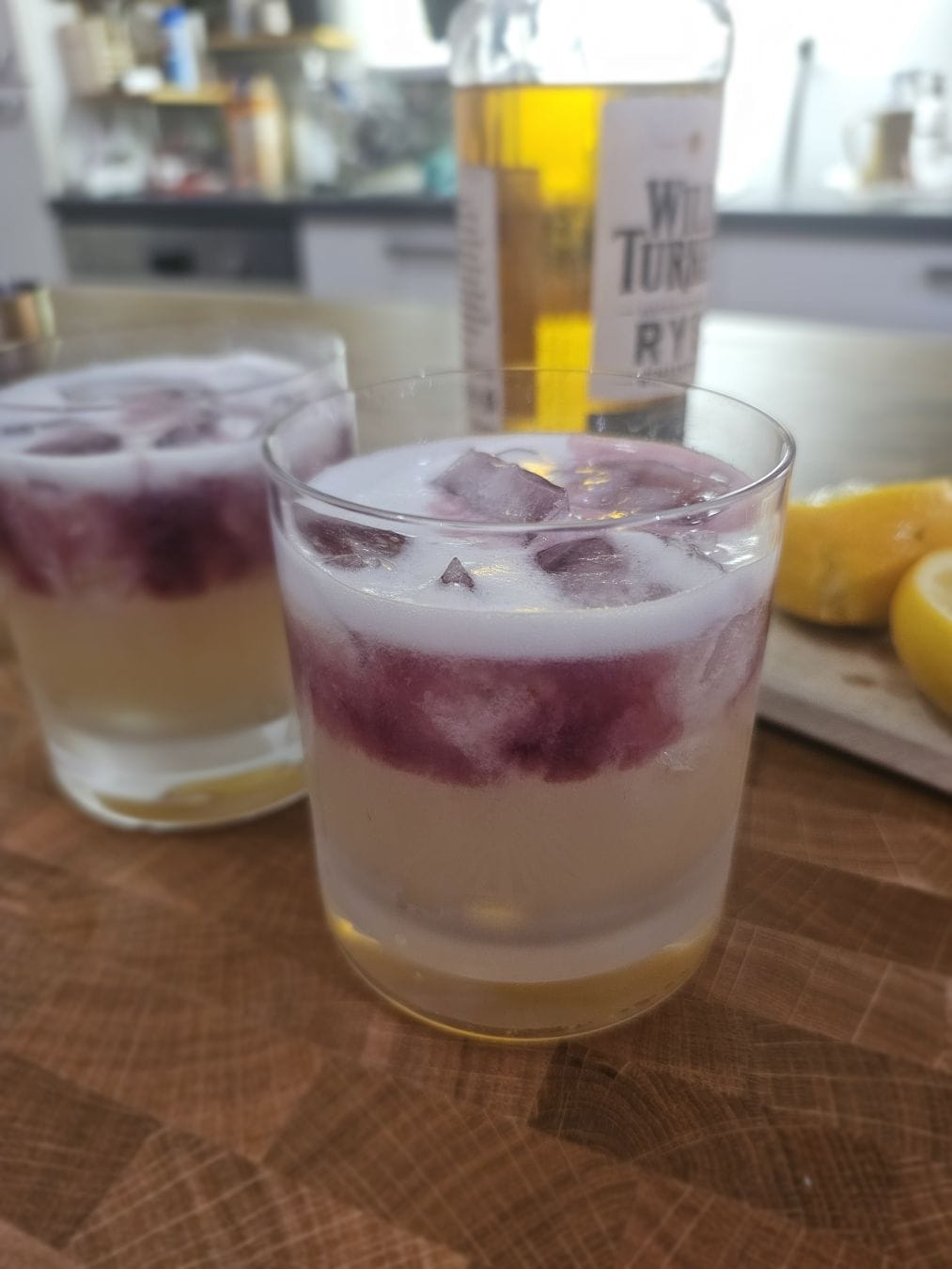 Two double old fashioned glasses filled with a lightly yellow liquid, with a red liquid floating on top.