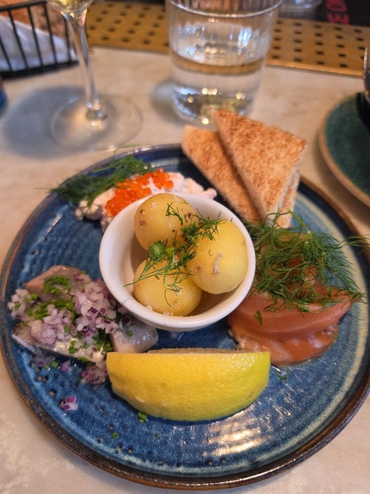 A blue plate with potatoes, salmon, herring, toast, roe, dill, and a lemon wedge.
