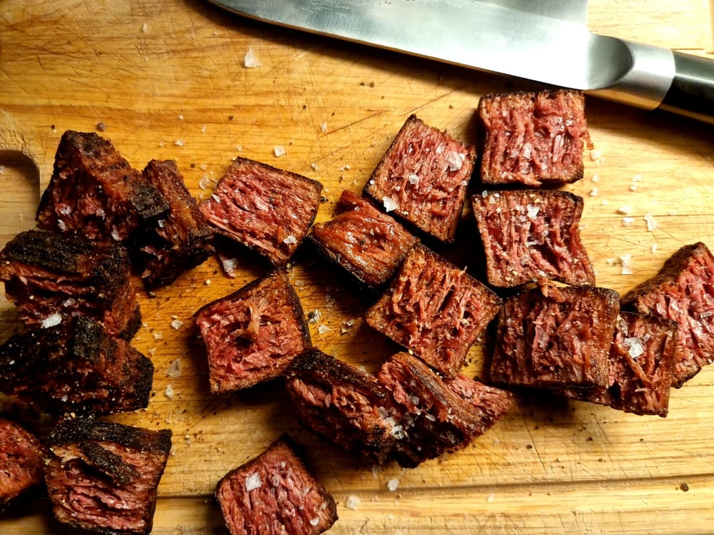 A wooden board with bite-sized pieces of fake meat, garnished with some salt-flakes.